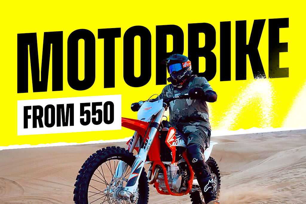 Person in protective gear riding a KTM dirt bike in the Dubai desert sand dunes