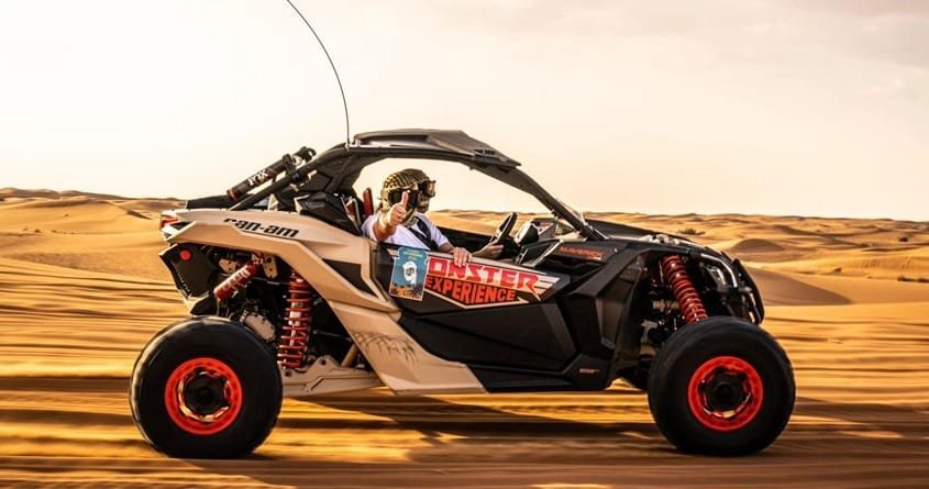 A man riding a black and red dune buggy in speed in the desert