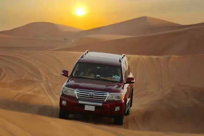 red color land cruiser in the desert with gorgeous backdrop of sunset in desert safari tour